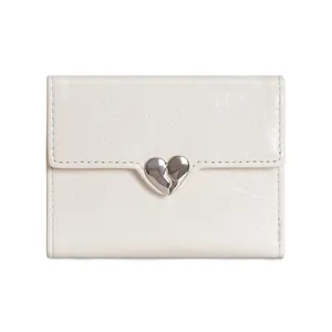 Close-up of cream tri-fold wallet featuring textured leather and a silver broken heart clasp