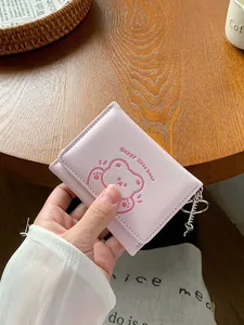Portafoglio rosa a tre ante con motivo a orsetto e portachiavi su un tavolo di legno