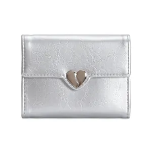 Detail of silver trifold wallet featuring wrinkled texture and metallic heart buckle