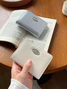 Minimalist wrinkled leather envelope wallets in silver and white on a wooden table