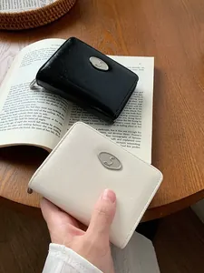 Mini portafogli con cerniera in ecopelle nera e beige su scrivania in legno chiaro