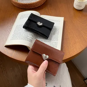 Minimalist heart buckle trifold wallet in black and brown leather on wooden table