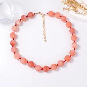 Détail du collier de perles rose pêche marbré avec cordon noué rouge et fermoir doré