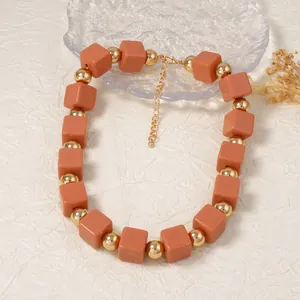 Vue détaillée des perles carrées brunes et des boules dorées sur un collier bohème