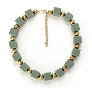 Détail de perles cubiques mates vertes et sphères dorées sur un collier bohème