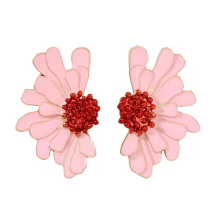 Détail macro des boucles d'oreilles fleurs en émail rose avec cœur perlé rouge sur fond blanc