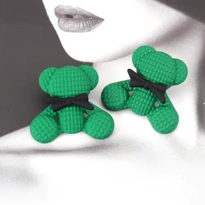 Orecchini a forma di orsetto verde con trama a nido d'ape e fiocchi neri su sfondo alla moda