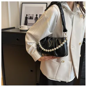 Detail of black pleated cloud bag featuring elegant white pearl chain and gold hardware
