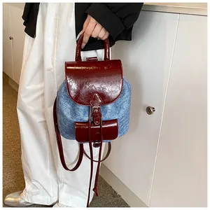 Detail of a mini denim backpack featuring red patent leather contrast and buckle closure