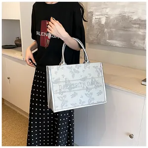 Detail of silver metallic tote bag featuring butterfly patterns and leather handles