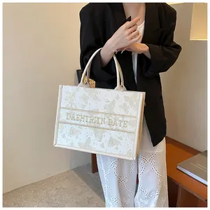 Detailed embroidery of gold butterflies on a cream canvas tote bag with top handles