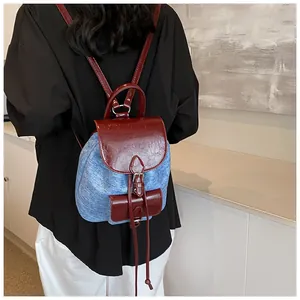 Rear view of a model wearing a mini denim and red PU leather backpack with silver hardware