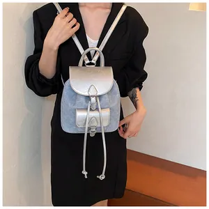 Detail view of denim and silver PU backpack featuring drawstring closure and flap buckle