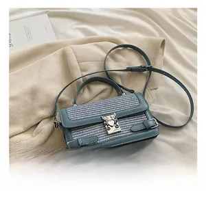 Detail of grey-blue woven leather bag with silver wing-heart clasp on white knit