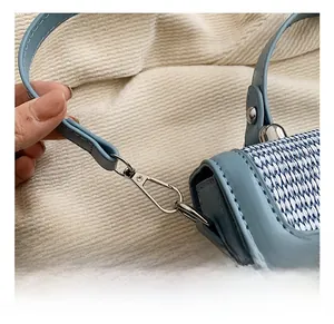 Close-up of a silver metal hook and woven blue fabric texture on a square handbag