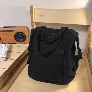 Close-up of black washed canvas backpack on a wooden chair showing the side buckle and handle