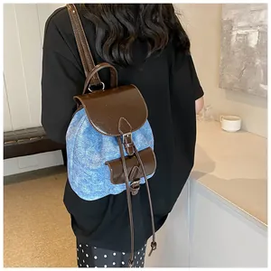 Rear view of a stylish denim and brown leather contrast backpack on a model in a cafe