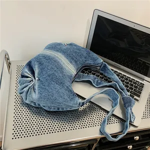 Detail of blue denim hobo bag with silver rivets and knotted strap on a metallic tray