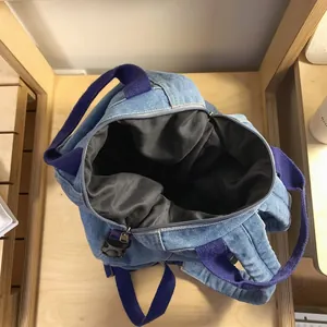 Detail of spacious interior lining and purple nylon straps on denim backpack