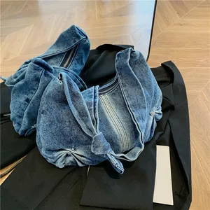 Detail of blue washed denim shoulder bag featuring a unique knotted strap and metal zipper