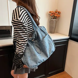 Große blaue Tote Bag mit Denim-Struktur und Kordelzug-Detail, lässig über der Schulter getragen