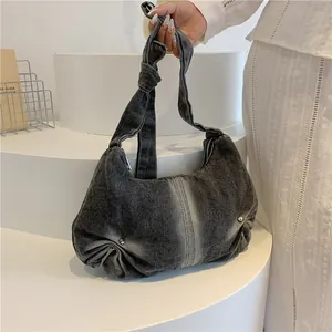 Detail of washed denim shoulder bag with knotted strap and metal rivet accents