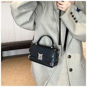 Detail of small black square bag with woven texture and silver metal lock on a model