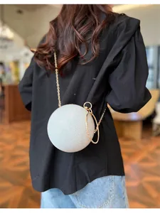 Détail d'un sac de soirée rond à paillettes argentées avec chaîne et poignée dorées
