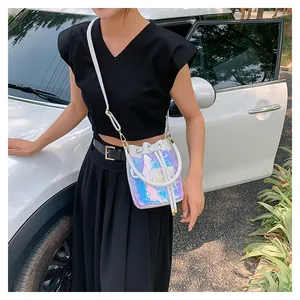 Détail du sac seau à paillettes irisées avec broderie The Cute sur étiquette en cuir blanc