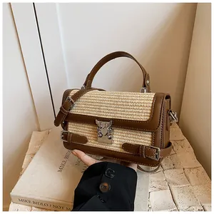 Detail of woven straw handbag with brown leather trim and silver butterfly metal clasp