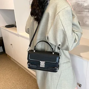 Minimalist black handbag with heart-shaped silver lock and textured flap on model's shoulder