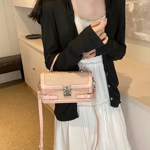 Pink woven mini square bag with heart lock being held by a model in a cozy setting