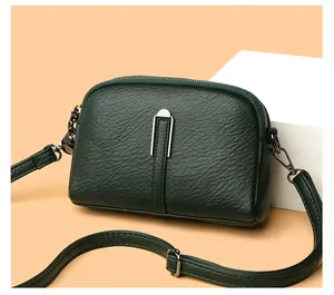 Detail of dark green crossbody bag with pebbled leather texture and silver hardware