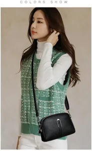 Close-up of black litchi grain leather shell bag with silver buckle worn on a green vest