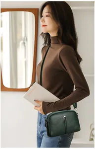 Detail view of dark green lychee grain leather crossbody bag with silver hardware on model