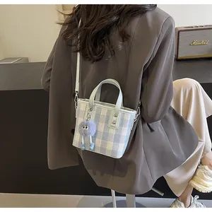 Detail of blue plaid bucket bag with plush monster charm and leather handle
