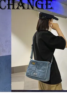 Close-up of blue denim shoulder bag featuring a large letter C patch and metal buckle