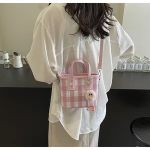 Detail of pink plaid mini tote bag with plush charm on a model in a cafe setting