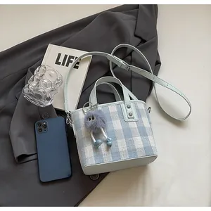 Flat lay of blue checkered canvas bucket bag with plush charm and lifestyle props