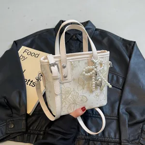 Chic beige bucket bag with gold butterfly print and pearl charm on black leather background