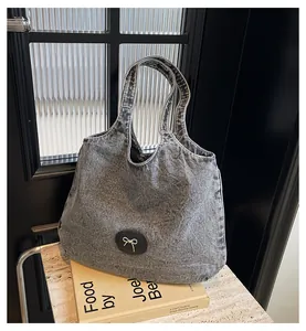 Detail of grey denim tote bag featuring a black leather patch with a silver bow ornament