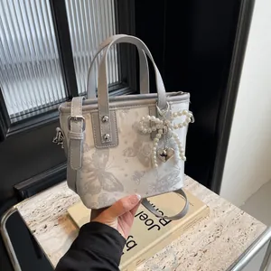 Light grey jacquard bucket bag with butterfly pattern and pearl heart charm held by hand