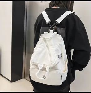 Rear view of a white canvas backpack with multi-zipper design worn by a model in a minimal setting
