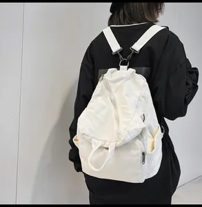Detail of white canvas backpack with Y-shaped metal buckle straps on black hoodie model