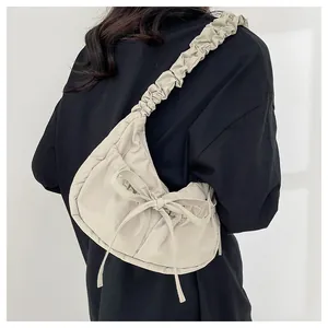 Detail of beige crescent shoulder bag featuring a large bow and ruffled adjustable strap