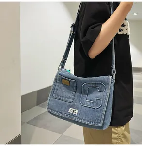 Detail of washed denim crossbody bag featuring a stitched letter C and metal twist lock