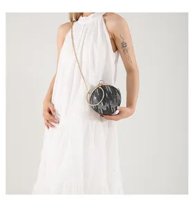Detail of round glitter evening bag with golden chain and ring handle on white dress