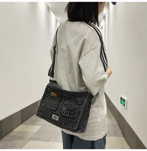 Detail of black washed denim crossbody bag featuring metal turn-lock and letter C patch