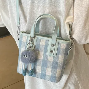 Blue and white plaid bucket bag with plush charm, showing elegant crossbody style