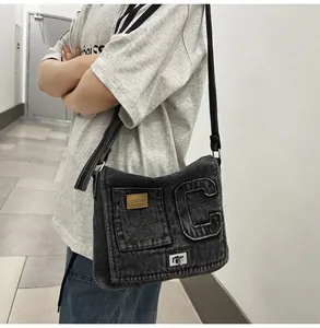 Detail of washed black denim crossbody bag with C letter patch and leather brand label